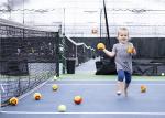 Enfant qui joue avec des balles sur un terrain de tennis intérieur